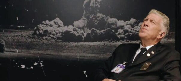 David Lynch as Gordon Cole in "Twin Peaks" season three, leaning back with his eyes closed and whistling while sitting in front of his desk